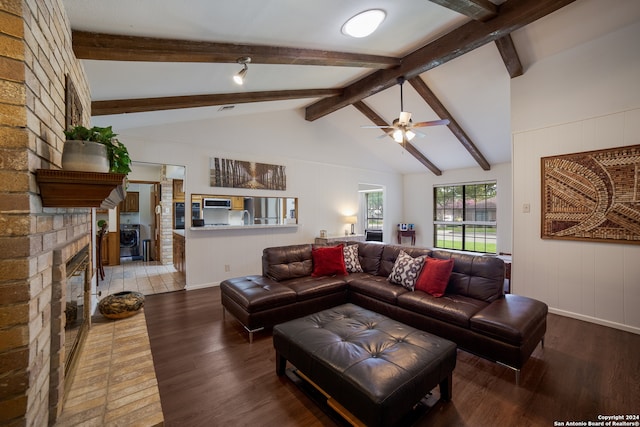 living room featuring vaulted ceiling with beams, dark wood-type flooring, ceiling fan, brick wall, and a fireplace