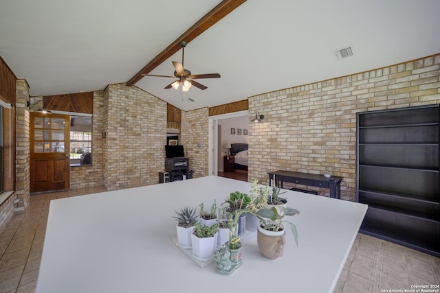 dining room featuring ceiling fan, brick wall, lofted ceiling with beams, and wood walls