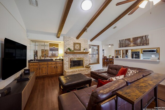 living room with a fireplace, ceiling fan, dark hardwood / wood-style flooring, brick wall, and lofted ceiling with beams