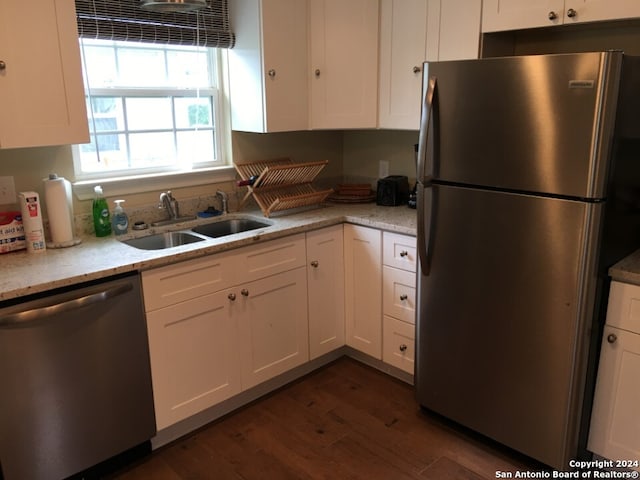 kitchen with appliances with stainless steel finishes, white cabinets, sink, light stone counters, and dark wood-type flooring