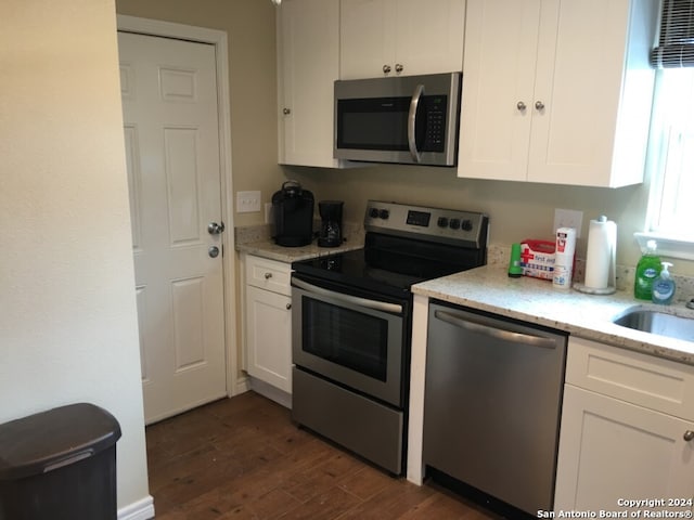 kitchen featuring appliances with stainless steel finishes, white cabinets, sink, light stone counters, and dark hardwood / wood-style floors