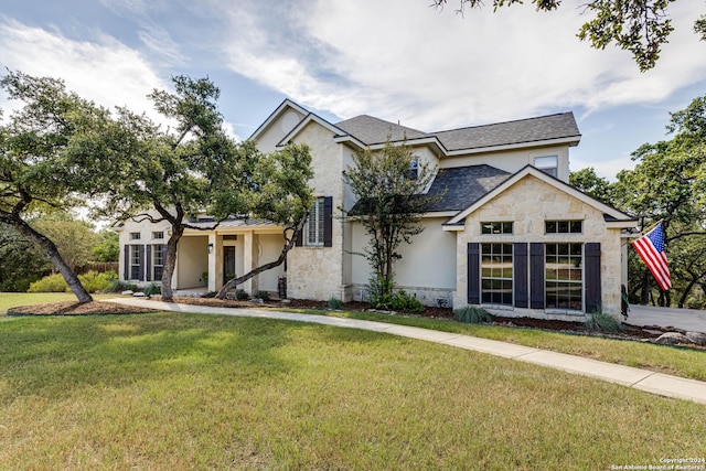 view of front of property with stone siding, a shingled roof, a front yard, and stucco siding