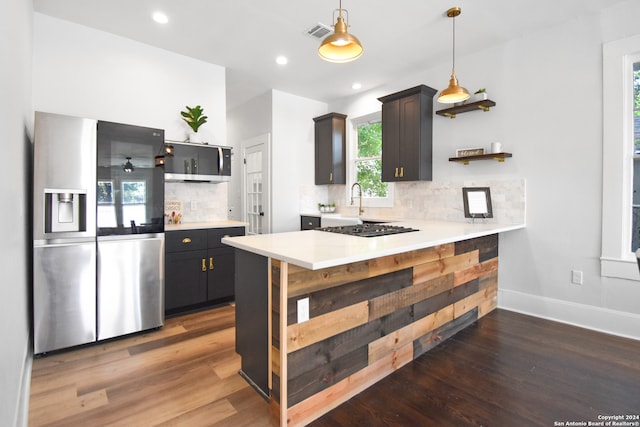 kitchen with stainless steel appliances, pendant lighting, decorative backsplash, hardwood / wood-style floors, and kitchen peninsula