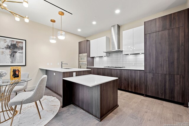 kitchen with light hardwood / wood-style flooring, dark brown cabinets, sink, kitchen peninsula, and pendant lighting