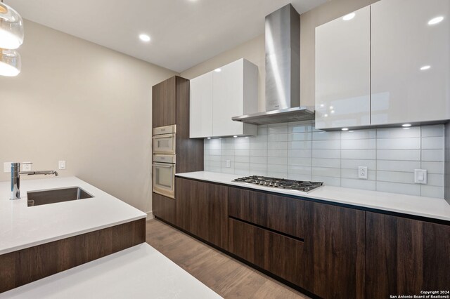 kitchen with white cabinets, stainless steel gas stovetop, light wood-type flooring, wall chimney exhaust hood, and backsplash