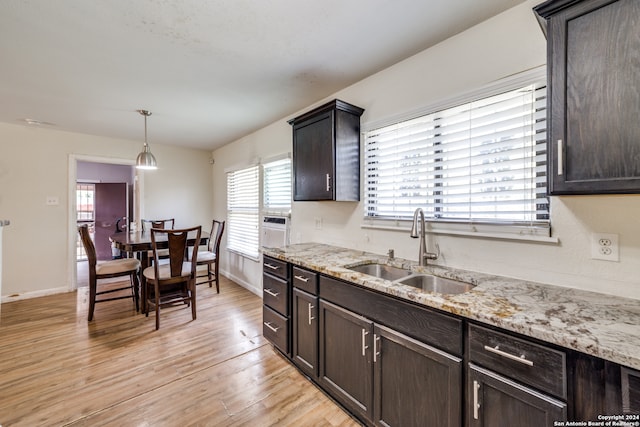 kitchen featuring light hardwood / wood-style flooring, light stone countertops, pendant lighting, dark brown cabinetry, and sink