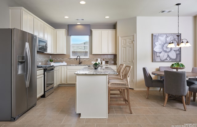 kitchen with stainless steel appliances, a center island, an inviting chandelier, hanging light fixtures, and light stone countertops