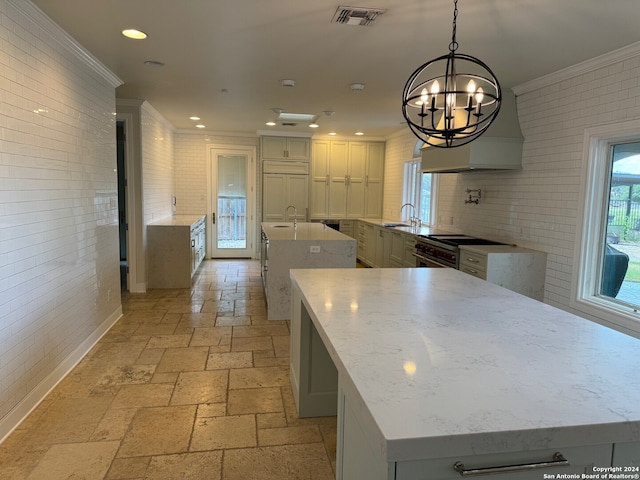 kitchen featuring light stone countertops, pendant lighting, crown molding, a center island, and a chandelier