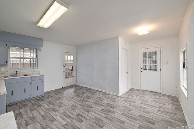 kitchen with gray cabinetry, sink, brick wall, and light wood-type flooring