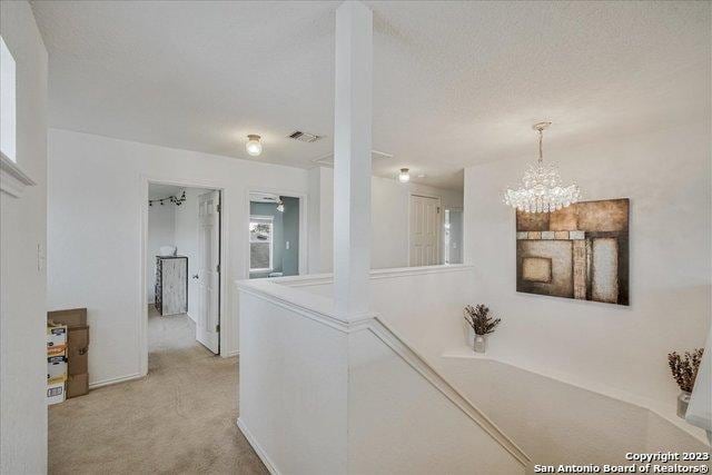 corridor featuring light colored carpet, a chandelier, and a textured ceiling