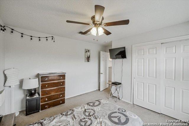 carpeted bedroom with ceiling fan, a closet, and a textured ceiling