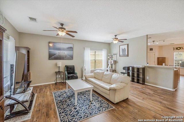 living room with wood-type flooring, ceiling fan, and a textured ceiling