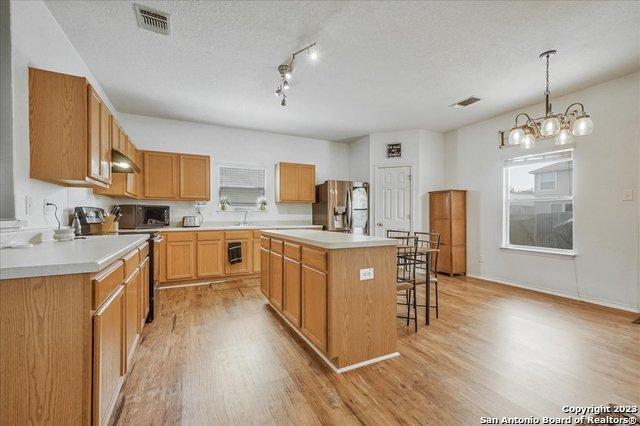 kitchen with pendant lighting, light hardwood / wood-style flooring, stainless steel appliances, and a kitchen island