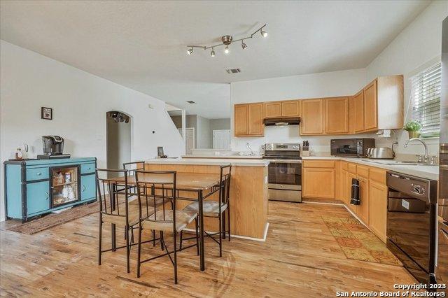 kitchen featuring light brown cabinetry, a breakfast bar area, light hardwood / wood-style flooring, dishwasher, and stainless steel electric stove