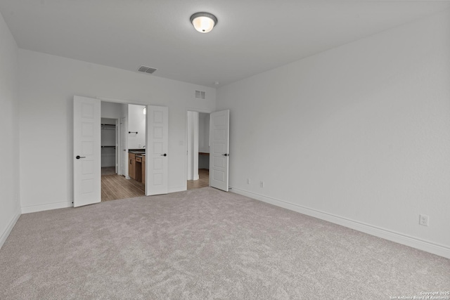 unfurnished bedroom featuring ensuite bathroom and light colored carpet