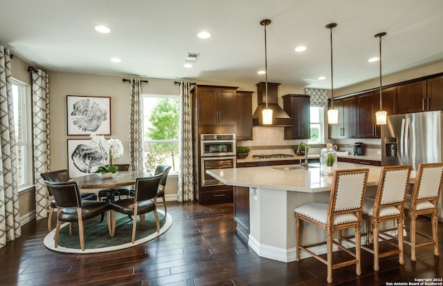 kitchen featuring pendant lighting, an island with sink, sink, custom exhaust hood, and stainless steel appliances