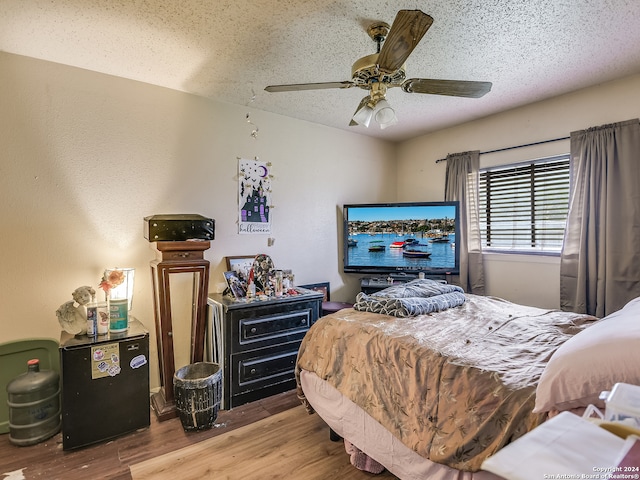 bedroom with a textured ceiling, fridge, wood-type flooring, and ceiling fan