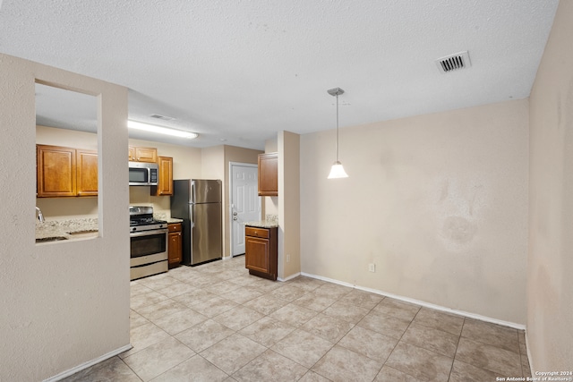 kitchen with pendant lighting, sink, light tile patterned floors, stainless steel appliances, and a textured ceiling