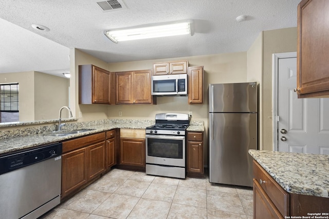 kitchen featuring stainless steel appliances, light stone countertops, sink, and light tile patterned floors