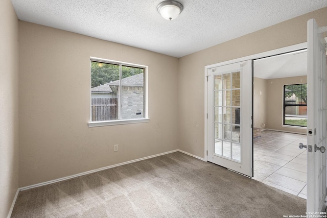 carpeted spare room with french doors, a textured ceiling, and a wealth of natural light