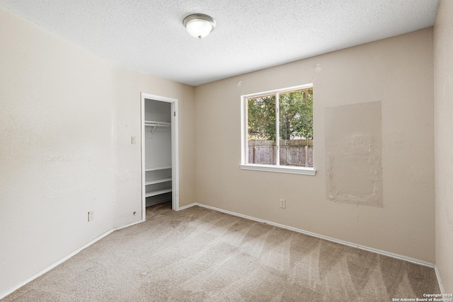 unfurnished bedroom featuring a walk in closet, a closet, a textured ceiling, and carpet flooring