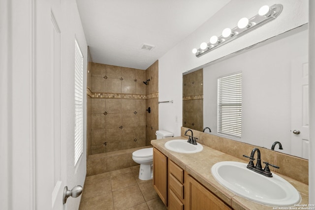 bathroom with tile patterned flooring, vanity, toilet, and tiled shower