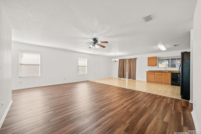 unfurnished living room featuring ceiling fan with notable chandelier, light hardwood / wood-style floors, sink, and a textured ceiling