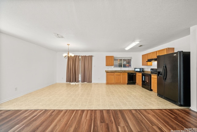 kitchen with hanging light fixtures, a chandelier, light wood-type flooring, and black appliances