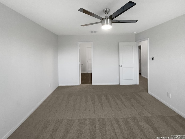 unfurnished bedroom with ceiling fan, ensuite bathroom, and dark carpet