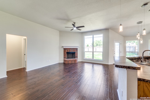 unfurnished living room featuring dark wood-type flooring, a brick fireplace, and a textured ceiling