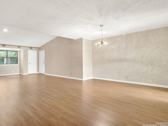 spare room with light hardwood / wood-style floors, vaulted ceiling, a chandelier, and a textured ceiling