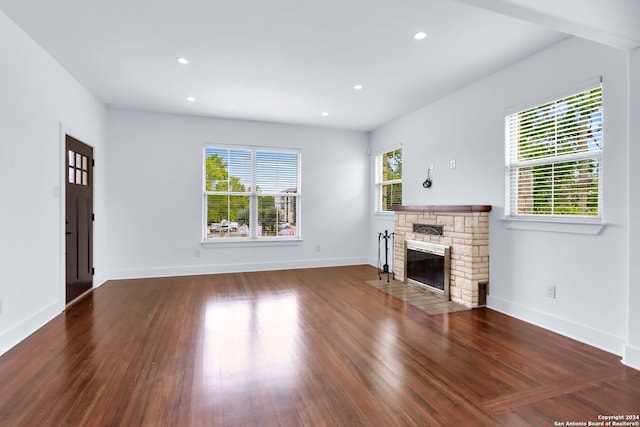 unfurnished living room with a stone fireplace and dark wood-type flooring