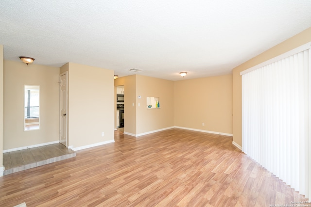 empty room with light wood-type flooring and a textured ceiling