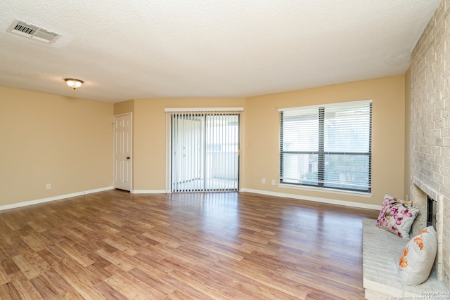 unfurnished living room featuring light hardwood / wood-style floors, a brick fireplace, and a textured ceiling