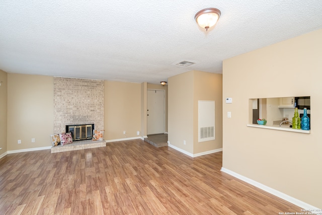 unfurnished living room with brick wall, a brick fireplace, light hardwood / wood-style flooring, and a textured ceiling