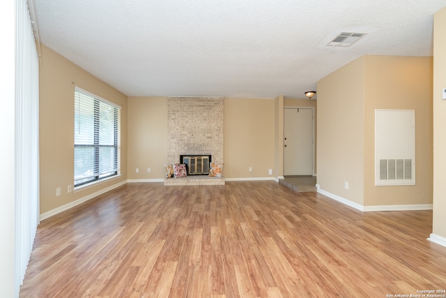 unfurnished living room featuring brick wall, a textured ceiling, a brick fireplace, and light hardwood / wood-style floors