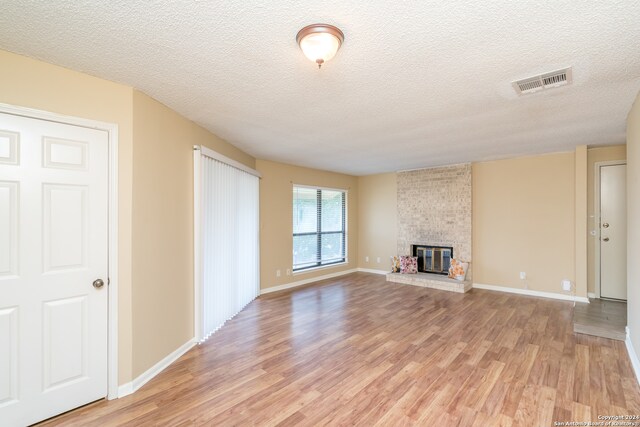 unfurnished living room with a fireplace, light hardwood / wood-style flooring, brick wall, and a textured ceiling