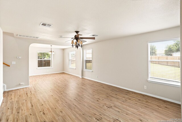 unfurnished room with a healthy amount of sunlight, a notable chandelier, wood-type flooring, and a textured ceiling