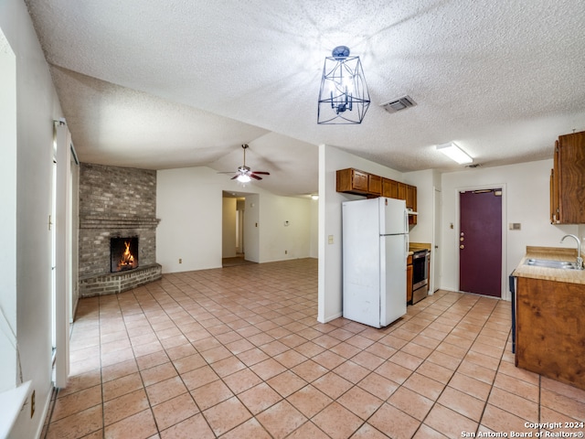 kitchen featuring ceiling fan, range with electric cooktop, a fireplace, white refrigerator, and sink