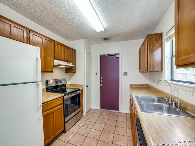 kitchen with white fridge, stainless steel electric stove, sink, a textured ceiling, and light tile patterned floors