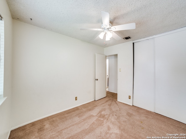 unfurnished bedroom featuring light carpet, a textured ceiling, a closet, and ceiling fan