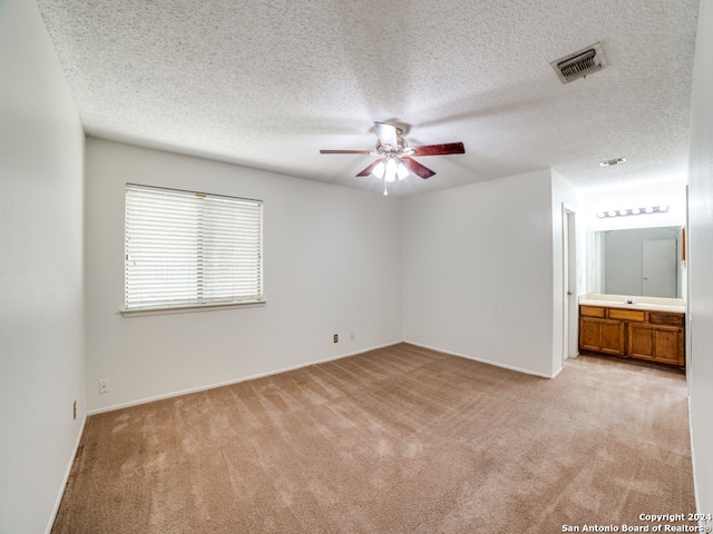 interior space featuring light carpet, ceiling fan, connected bathroom, and a textured ceiling