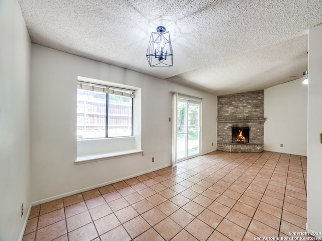 unfurnished living room featuring light tile patterned floors, a textured ceiling, ceiling fan, brick wall, and a fireplace