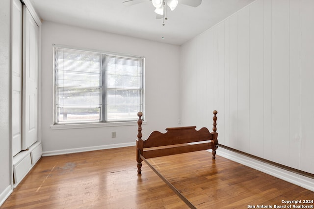 bedroom featuring wooden walls, wood-type flooring, and ceiling fan