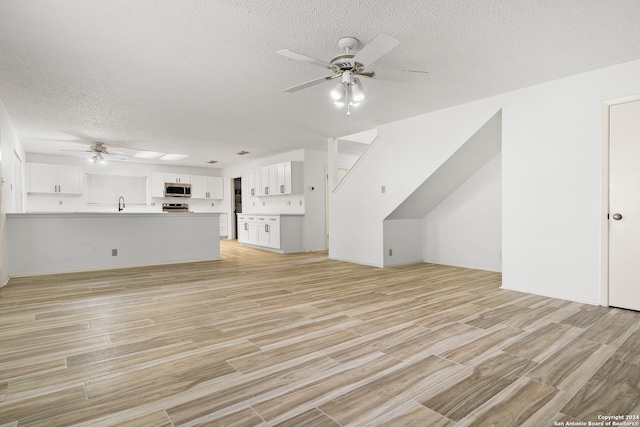 unfurnished living room featuring a textured ceiling, ceiling fan, and light wood-type flooring