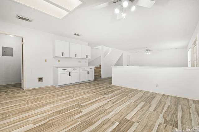 unfurnished living room with light wood-type flooring, ceiling fan, a skylight, and electric panel