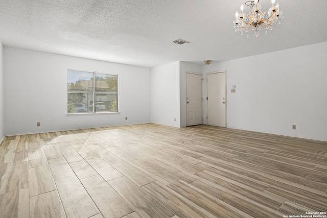 spare room with light hardwood / wood-style floors, a notable chandelier, and a textured ceiling