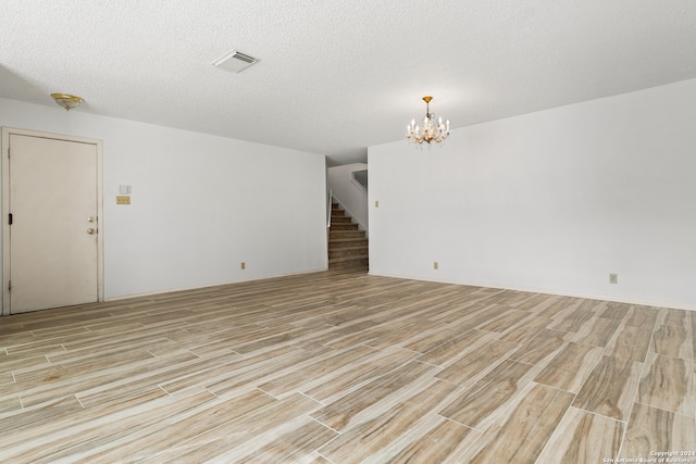 spare room with a notable chandelier, a textured ceiling, and light hardwood / wood-style floors