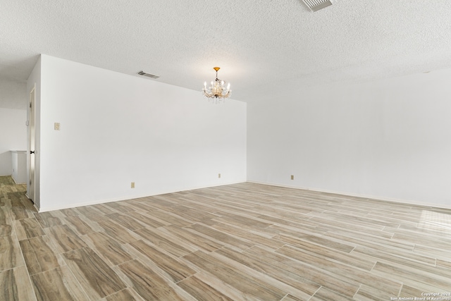 empty room with light hardwood / wood-style floors, an inviting chandelier, and a textured ceiling