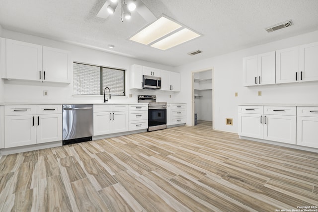 kitchen featuring white cabinetry, ceiling fan, appliances with stainless steel finishes, light hardwood / wood-style flooring, and a textured ceiling